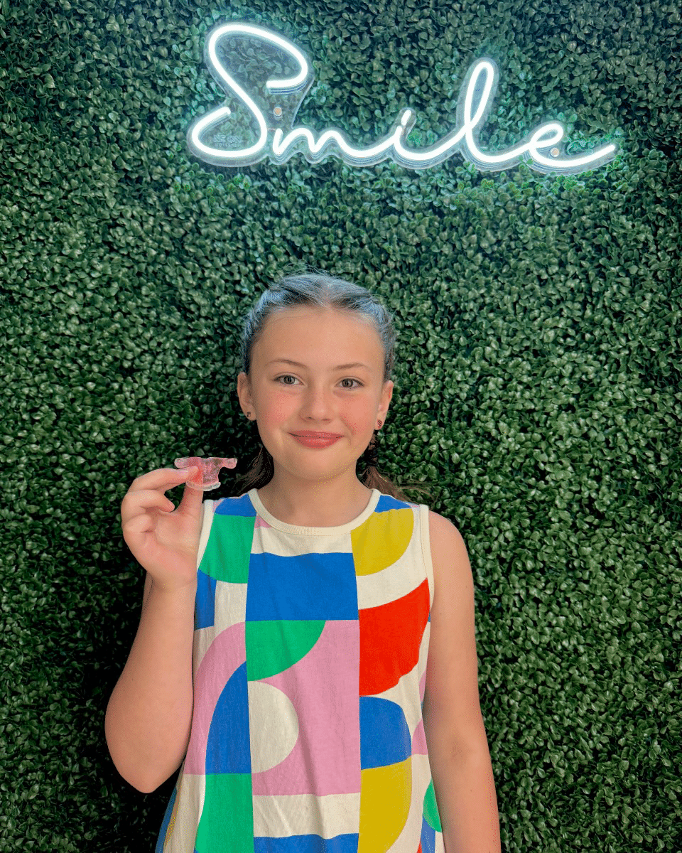 Happy young patient holding her Phase 1 retainer at Giardina Orthodontics in Harrisonburg, showing successful early orthodontic treatment results