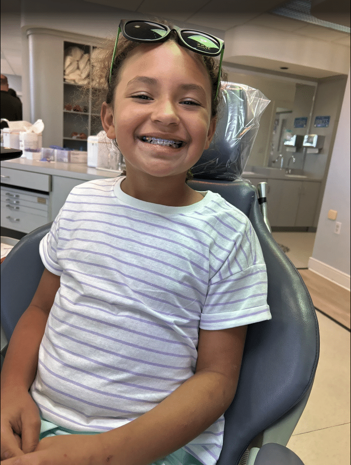 Smiling young girl with colorful braces sitting in dental chair at Giardina Orthodontics family-friendly office in Harrisonburg, VA