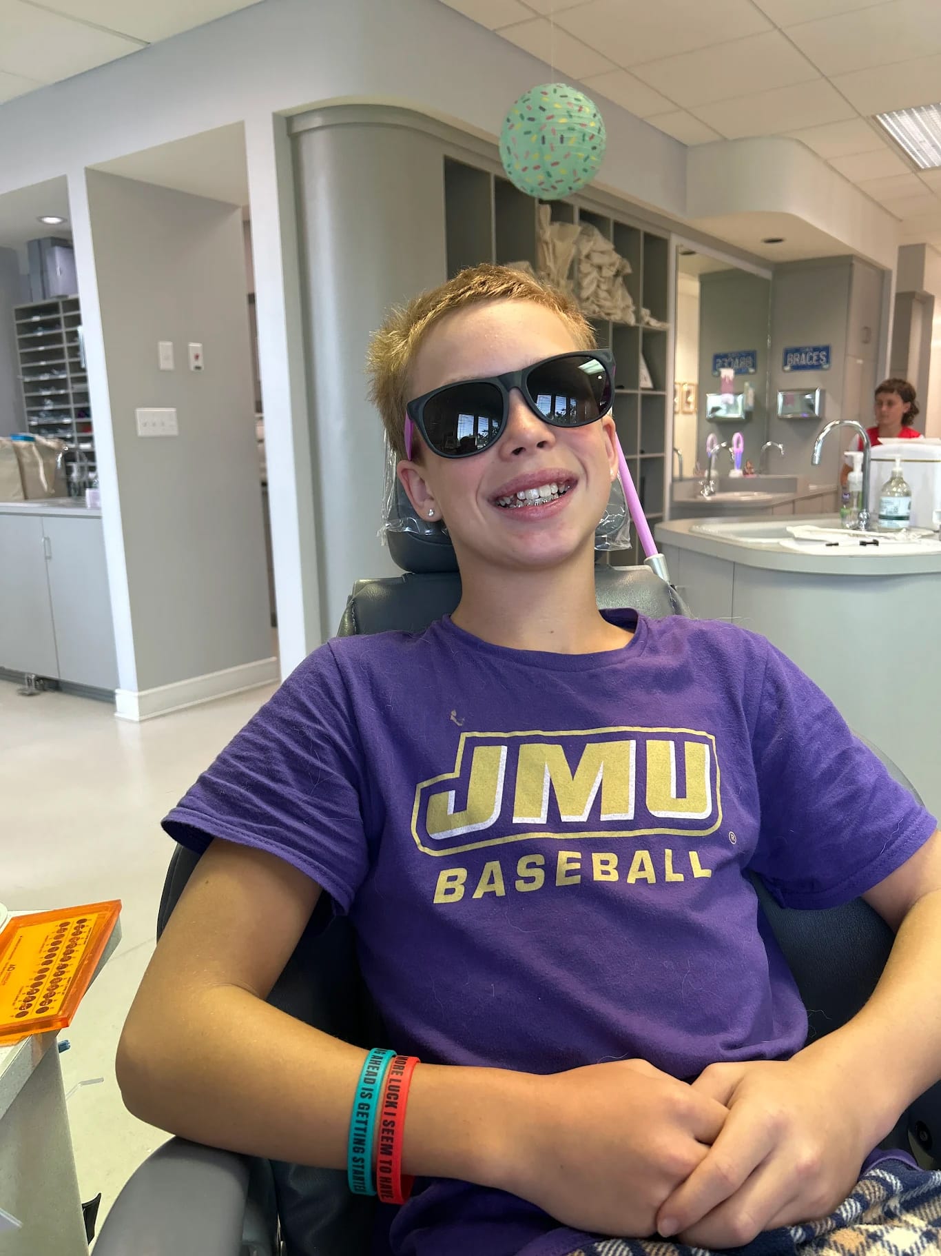 Smiling teenage patient wearing JMU shirt and sunglasses during orthodontic treatment at Giardina Orthodontics modern office in Harrisonburg, VA