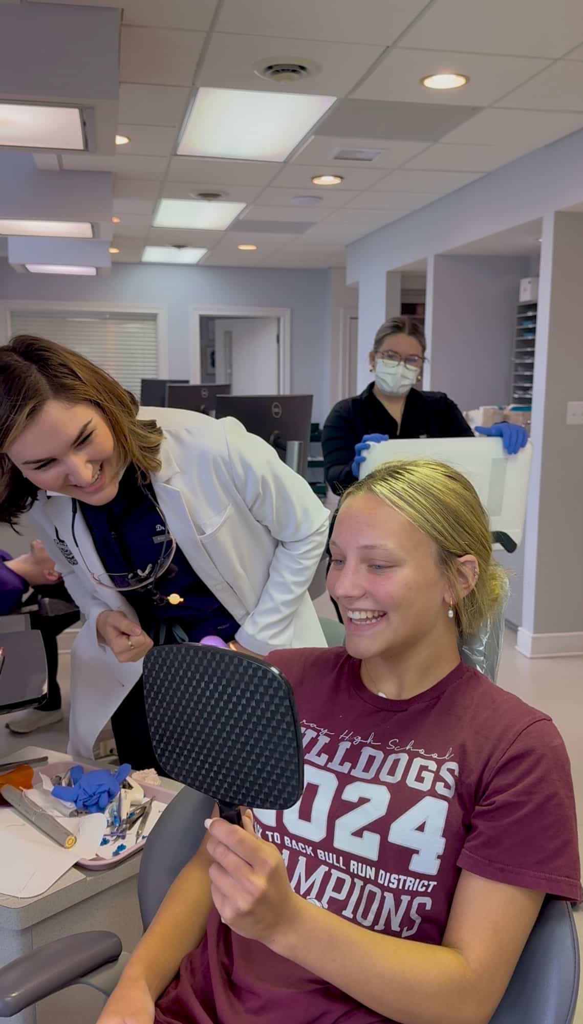 Female high school athlete checking her smile with braces at Giardina Orthodontics in Harrisonburg, VA while wearing her team championship shirt