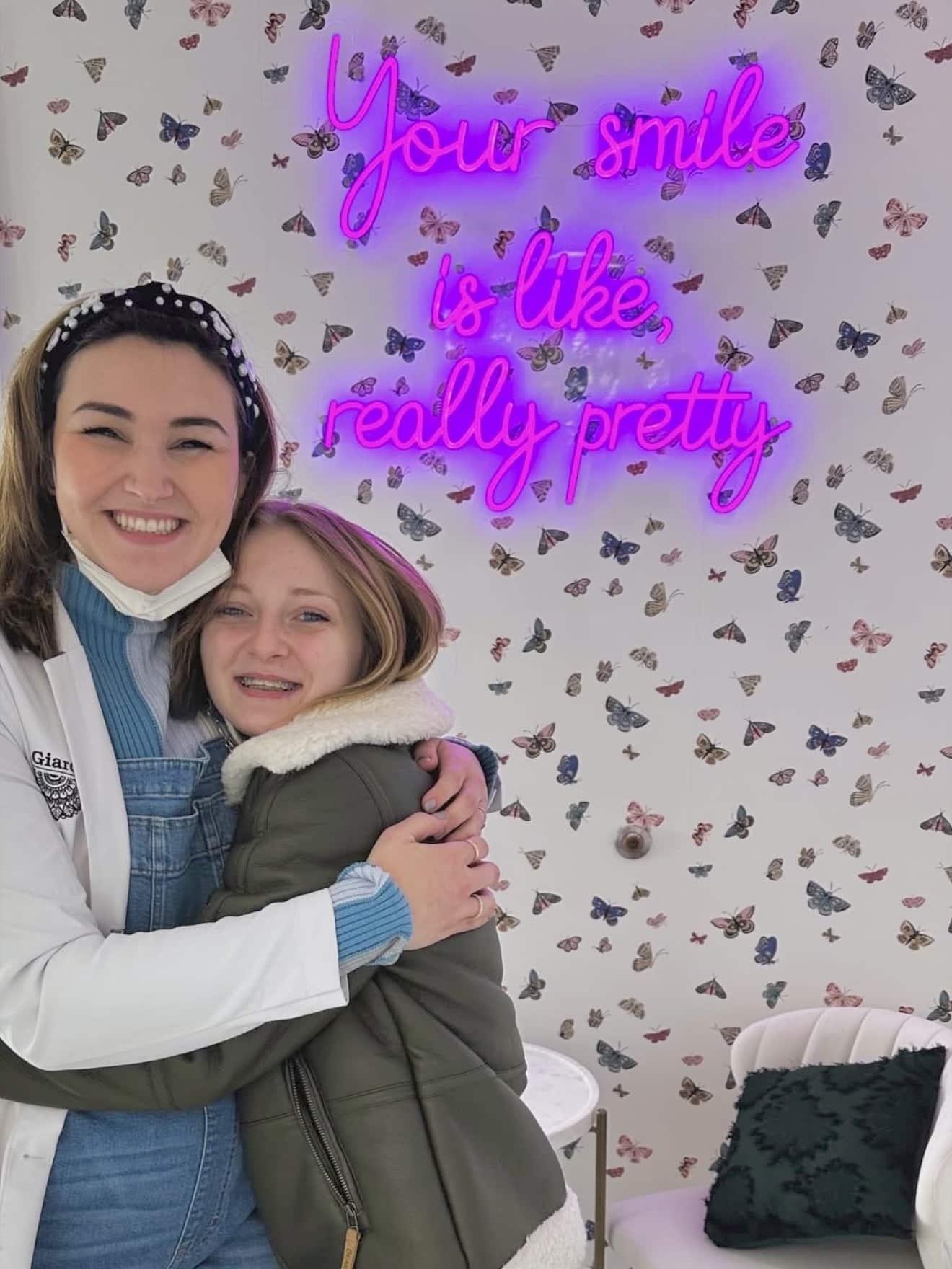 Giardina Orthodontics team member hugging a happy teen patient in front of the butterfly wallpaper and neon sign at the Harrisonburg VA office where families get braces