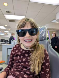 Smiling young girl with braces wearing protective sunglasses in the chair at Giardina Orthodontics in Harrisonburg, VA